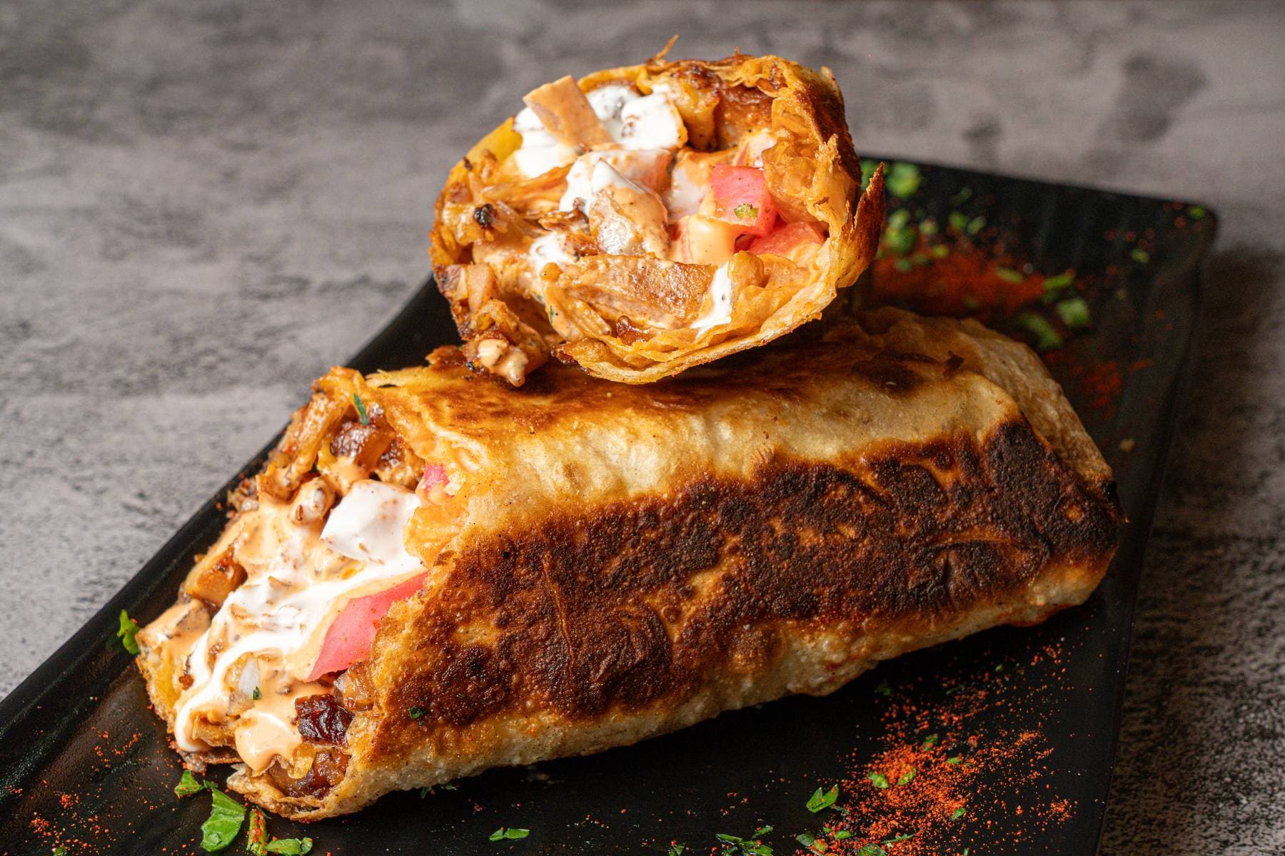 Chicken shawarma laffa wrap, halved to show the filling: marinated chicken, pickles, tahini