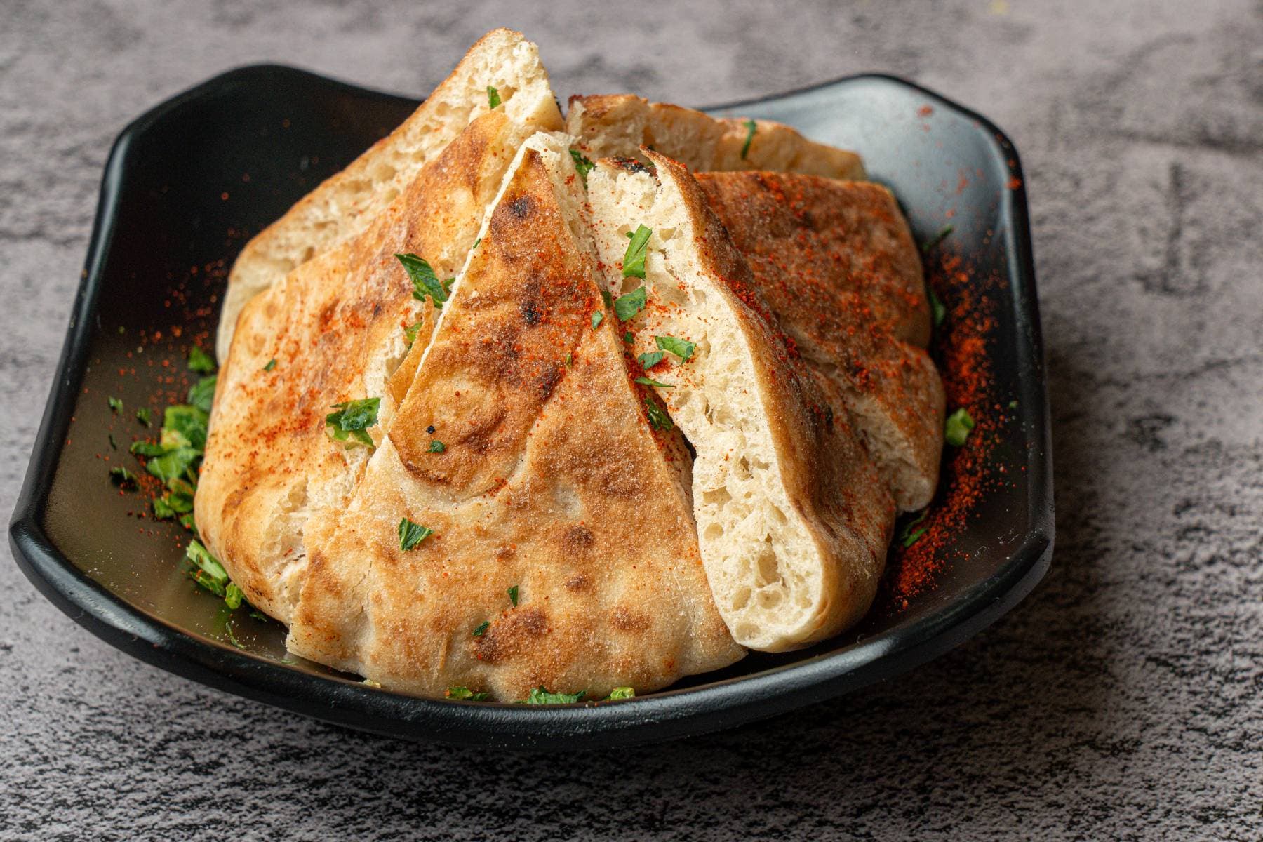 Egyptian hawashi served in a black bowl, the crisp flatbread split open and dusted with paprika and parsley